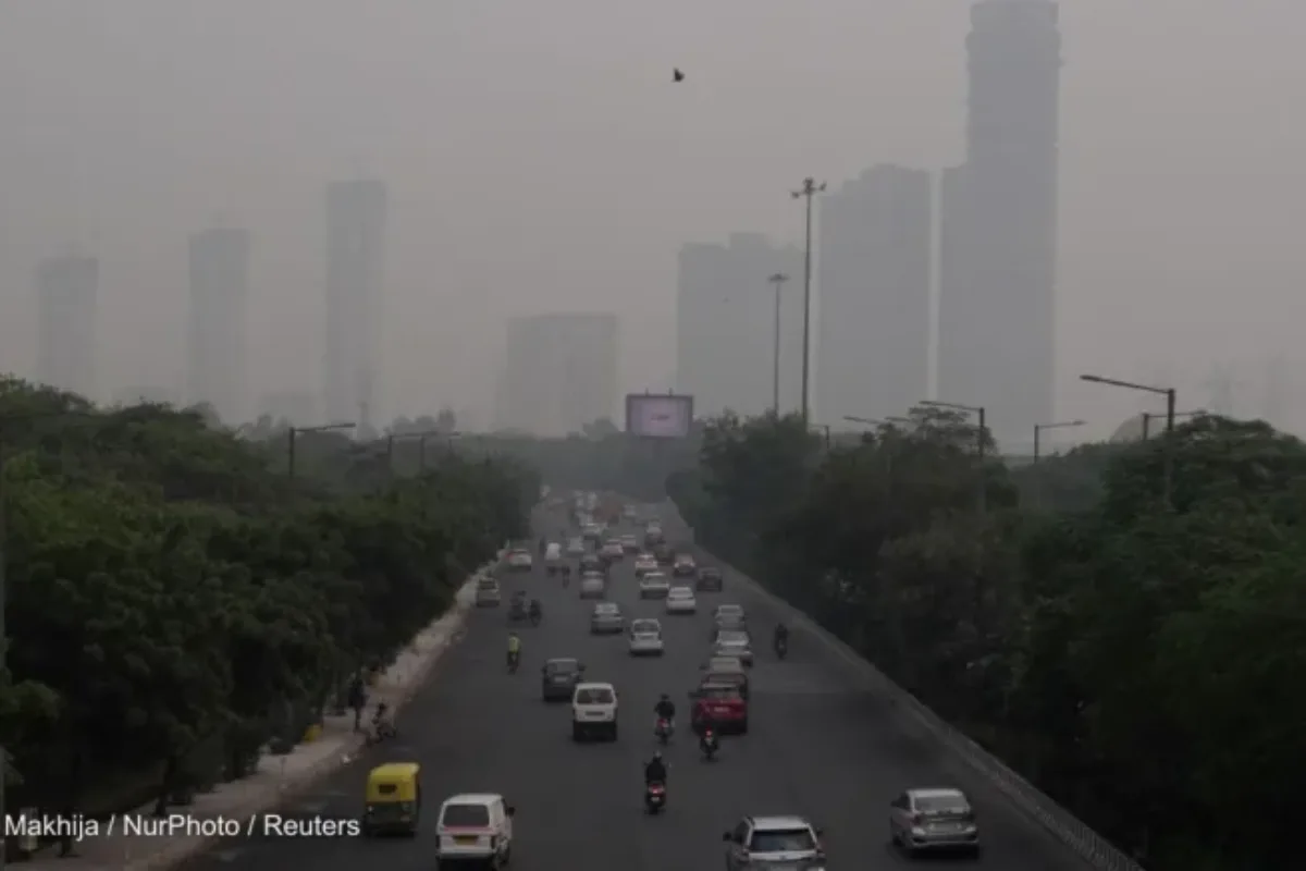 Cars drive on a wide road toward a city shrouded in smog
